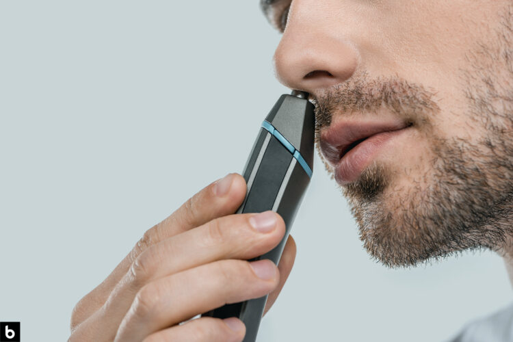 This is the cover photo for our Best Nose Hair Trimmer article. It features a man with facial scruff using a black and blue nose hair trimmer to shave his nose.