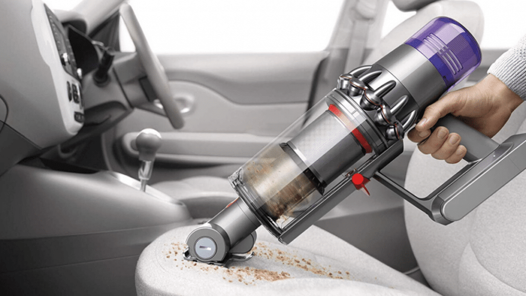 This is a picture of a person using a Dyson cordless vacuum to clean their car interior.