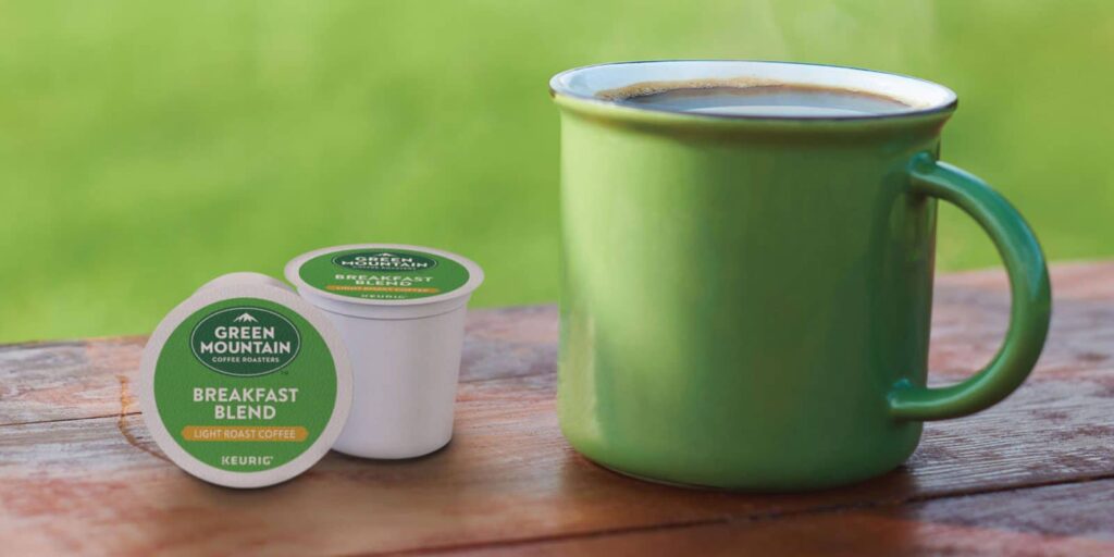 This is a photo of a green mug filled with coffee placed on a wooden table with two k-cups placed next to it.