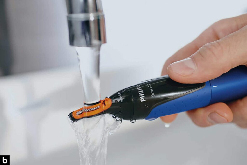 This is an image of a person washing a nose hair trimmer under the water to clean it.