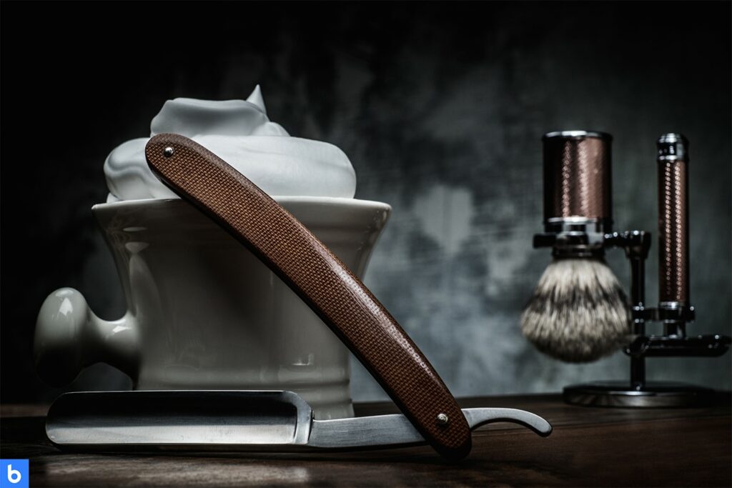 This is a photo of a shaving kit placed on a table. It includes shaving cream, an application brush, and a straight razor.