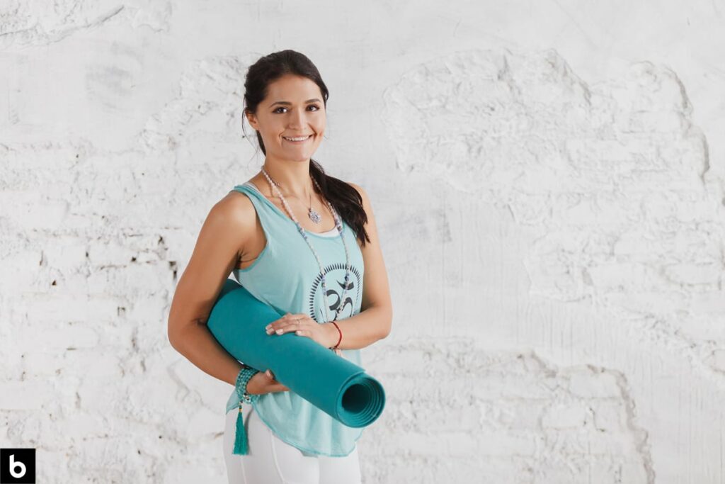 This is an image of a woman holding a yoga mat, dressed in workout apparel.