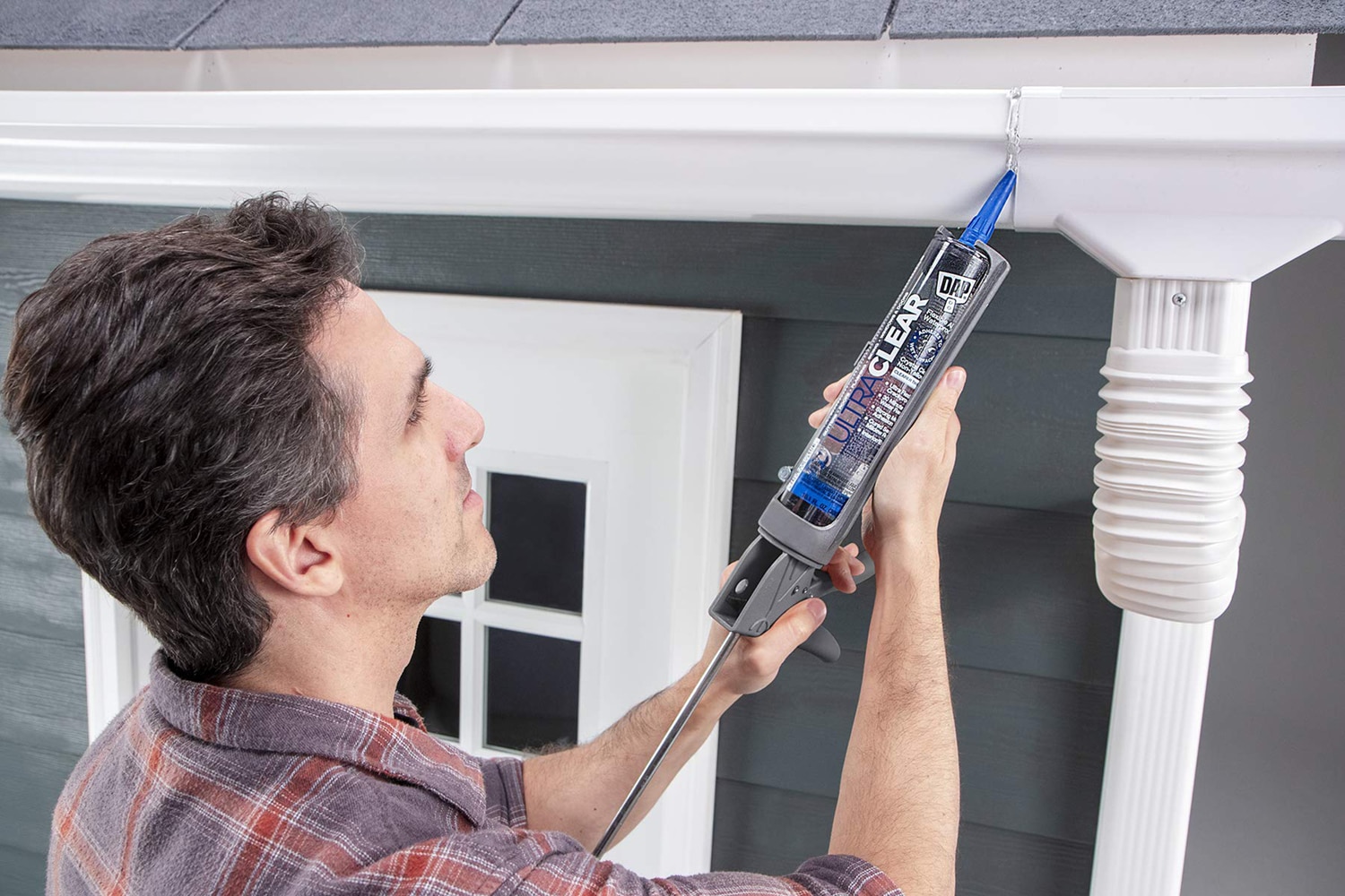 This is the cover photo for our Best Caulking & Sealants article. It shows a man using a caulking gun to seal a gutter.