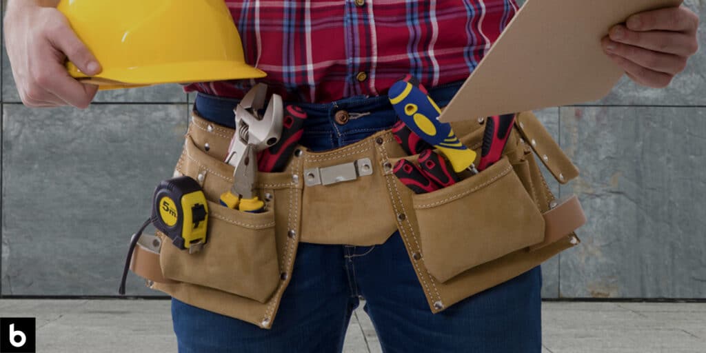 This is a photo for our Tool Belt Buying Guide. It shows a man holding a clipboard and a hard hat, and wearing a tool belt with various tools inside.