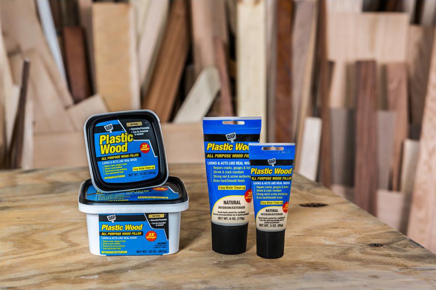 This is the cover photo for our Best Wood Filler article. It shows several tubes and buckets of wood filler on top of a wooden table and various wood scraps in the background.
