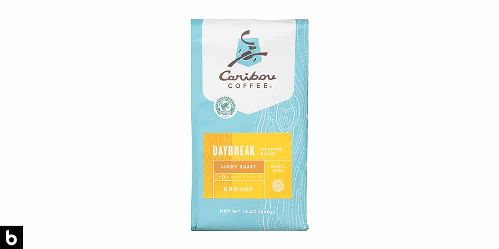 This is a product image, featuring a blue and yellow bag of Caribou Coffee Daybreak Light Roast coffee.