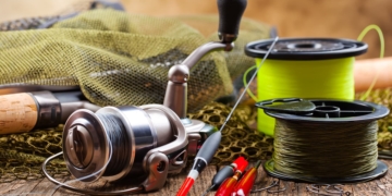 This is the cover photo for our Best Braided Fishing Line article. It features a couple spools of braided fishing line on a table, with a fishing rod, and assorted fishing tackle.
