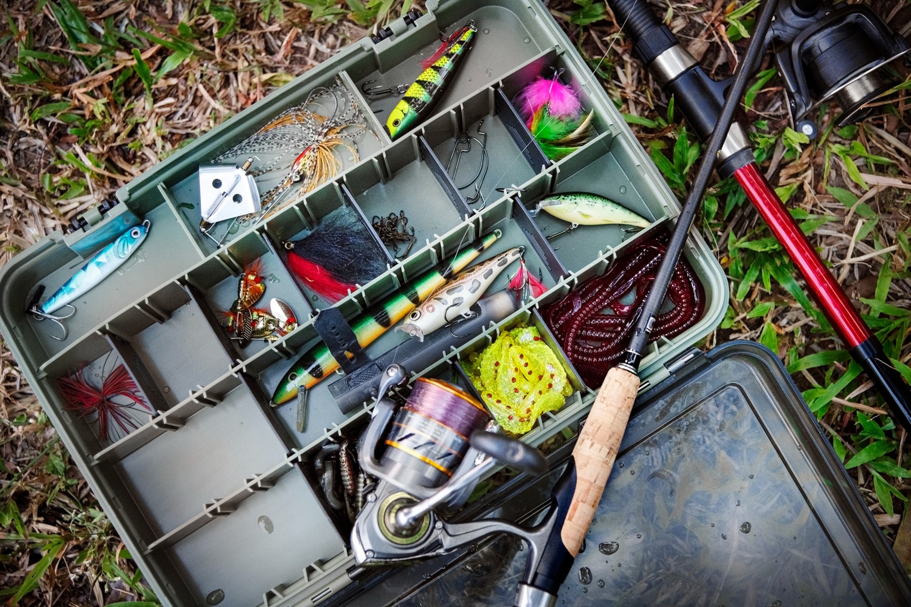 This is the cover photo for our Best Tackle Box article. It features a tackle box on the ground with fishing lures and assorted accessories inside.
