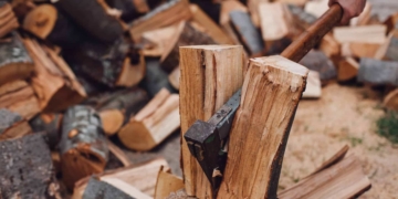 This is the cover photo for our Best Wood Splitting Axe article. It features an axe splitting a log with a pile of split wood in the background.